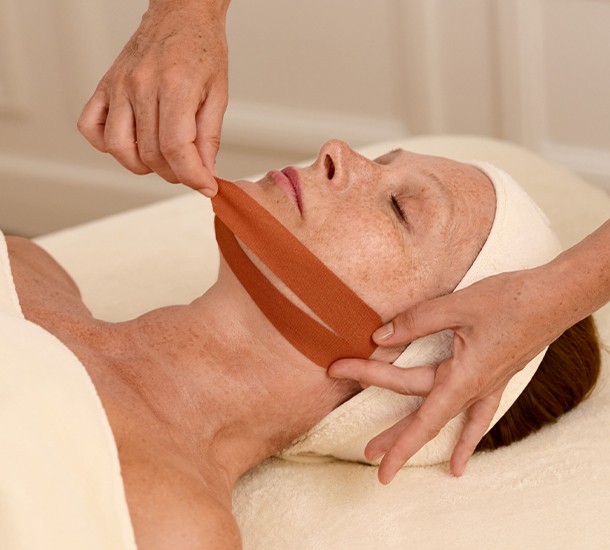 Application de bandes de face tape esthétique sur le visage d'une femme lors d'une formation de face taping