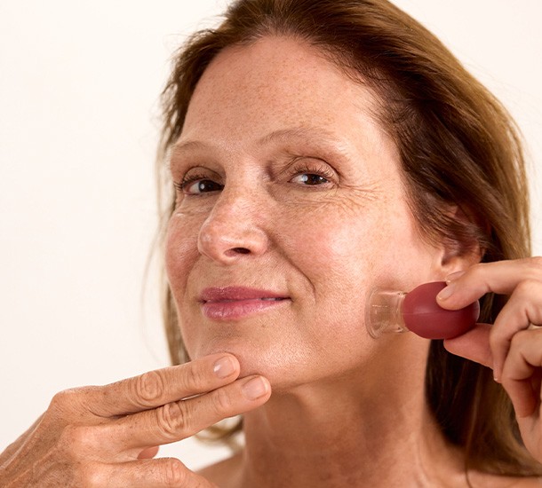 Femme appliquant une ventouse de massage en verre LB Facialistes sur sa joue pour drainer et raffermir
