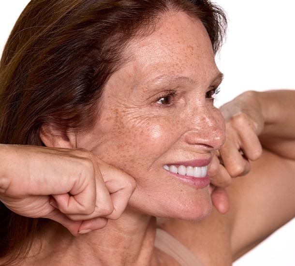 Femme souriante utilisant ses articulations pour masser la ligne de sa mâchoire de profil